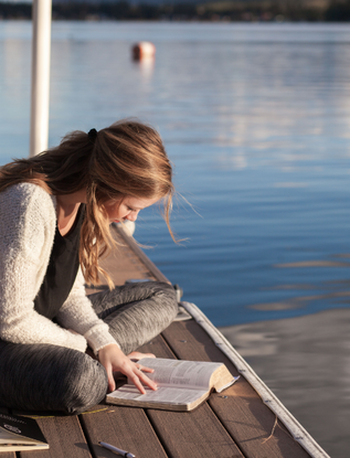 Summer School: ein Mädchen liest am Seeufer ein Buch.